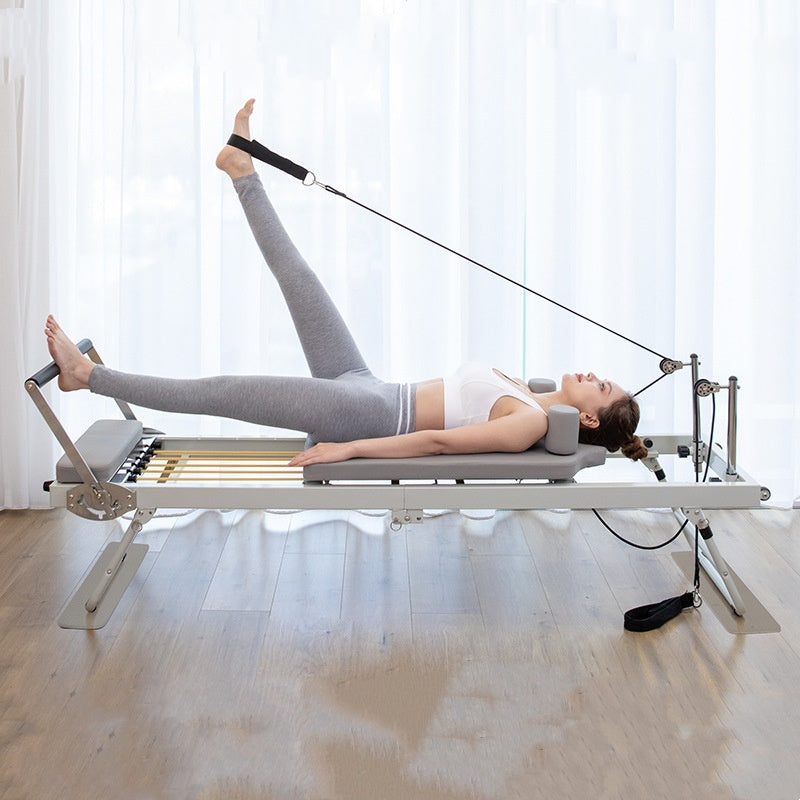 Woman using a Pilates reformer machine with resistance bands in a bright room.